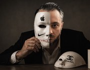 Мужчина в костюме держит маску с логотипами Apple и Nike, рядом — надпись Tesla и предметы с логотипами Chanel и Louis Vuitton